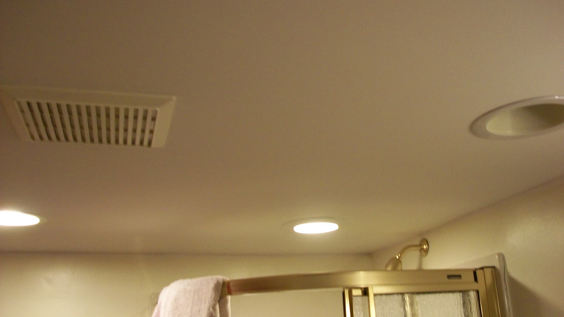 Bathroom ceiling with a rectangular exhaust vent above a shower enclosure
