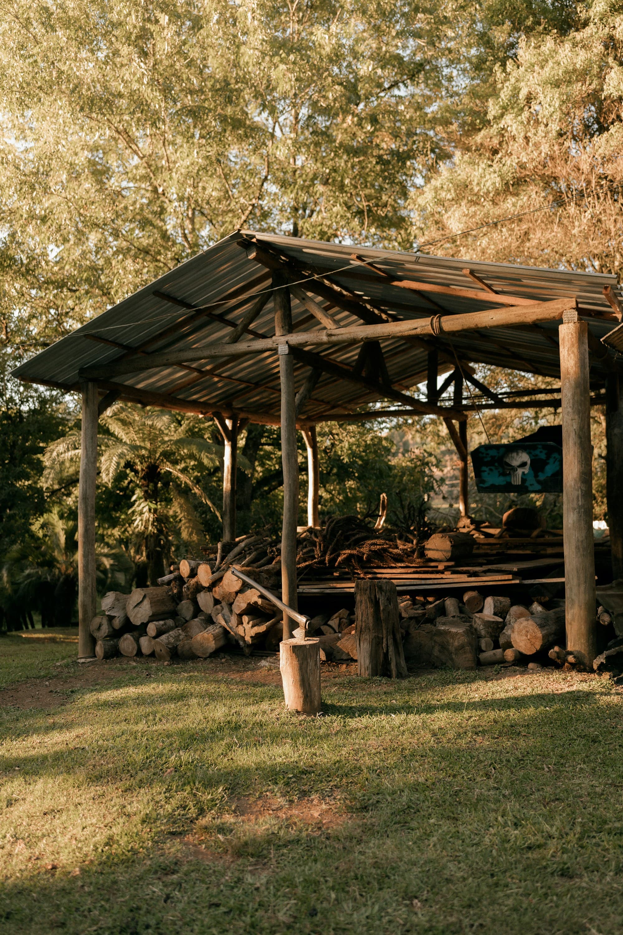 Split firewood stacked under an open-sided wooden shelter in a grassy field